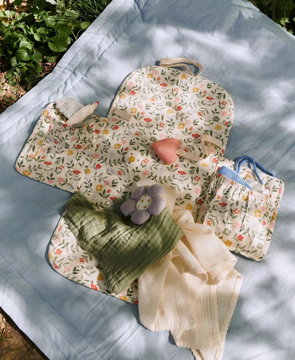 Dear April verschoonmat met bloemenprint, hydrofiele doeken, speentjeslint en zachte knuffels uitgestald op een lichtblauwe deken buiten